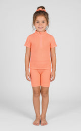 Coral ribbed seamless short-sleeve top with quarter zip and matching mid-thigh shorts on toddler girl with pink hair tie.
