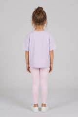 Toddler wearing pale pink leggings with a lavender T-shirt, shown from behind with white sneakers.