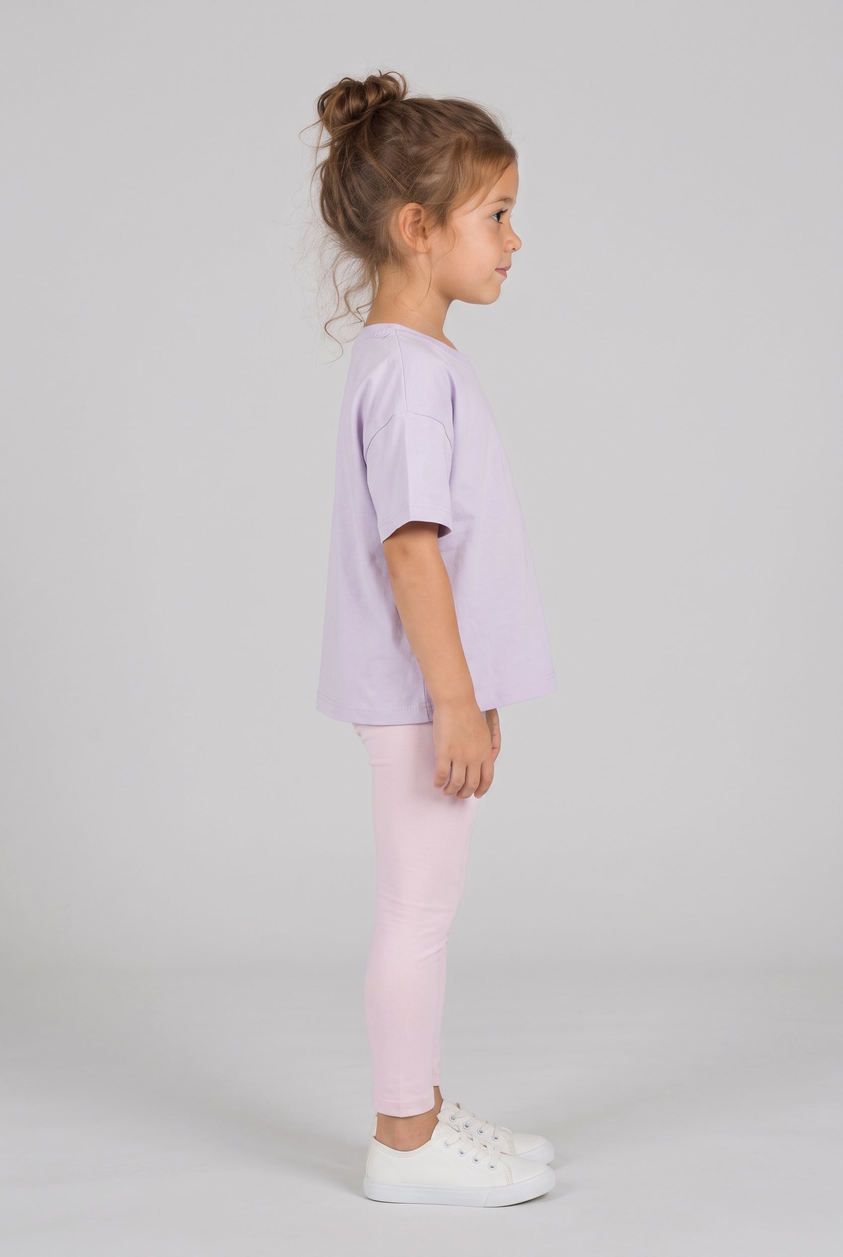 Toddler wearing a light lavender oversized T-shirt with pale pink leggings and white sneakers, shown in side profile.