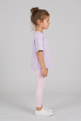 Toddler wearing a light lavender oversized T-shirt with pale pink leggings and white sneakers, shown in side profile.