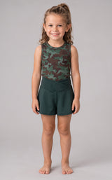 Little girl wearing sleeveless green camouflage tank top with solid dark green crossover athletic shorts.