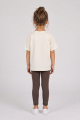 Toddler wearing slim dark gray leggings with a cream short-sleeve top and white sneakers, shown from behind.
