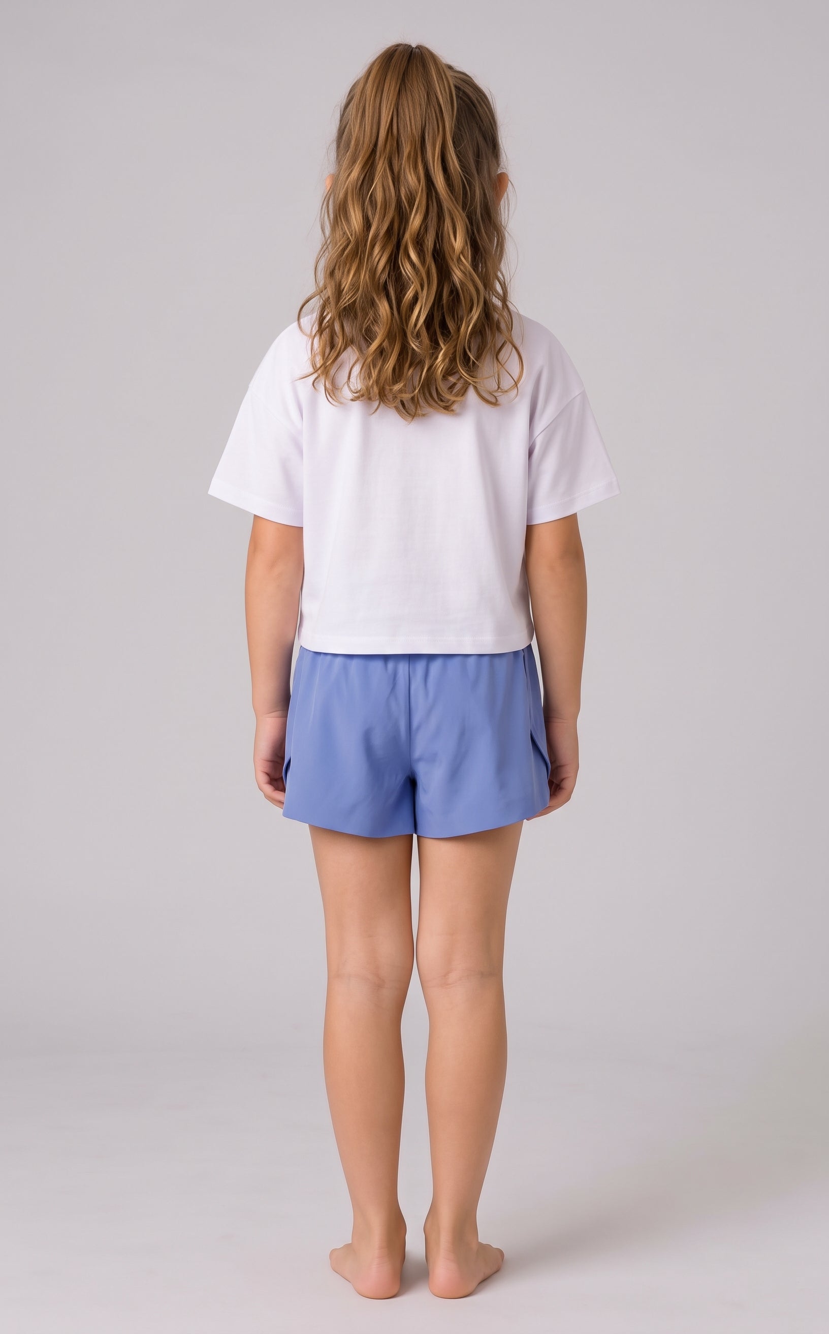 Back view of a girl wearing periwinkle blue running shorts with fluttered outer panels and a white T-shirt.