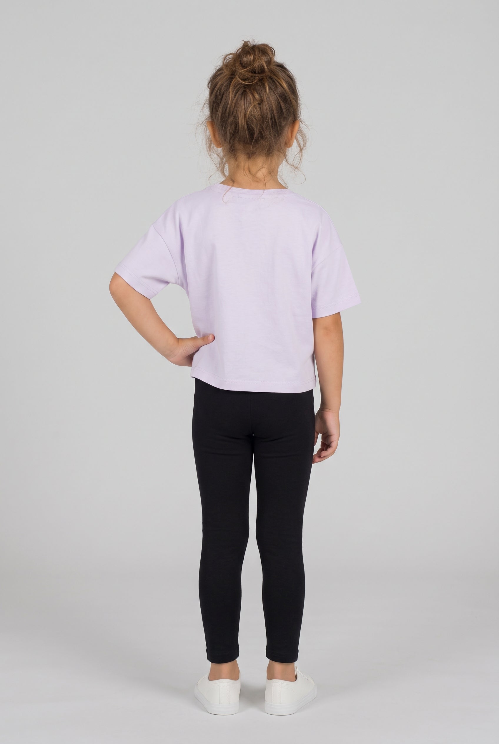 Toddler wearing a pale lavender short-sleeve shirt with fitted black leggings and white sneakers, shown from behind.