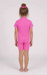 Back view of a toddler girl wearing a bright pink ribbed short-sleeve top and matching fitted shorts.