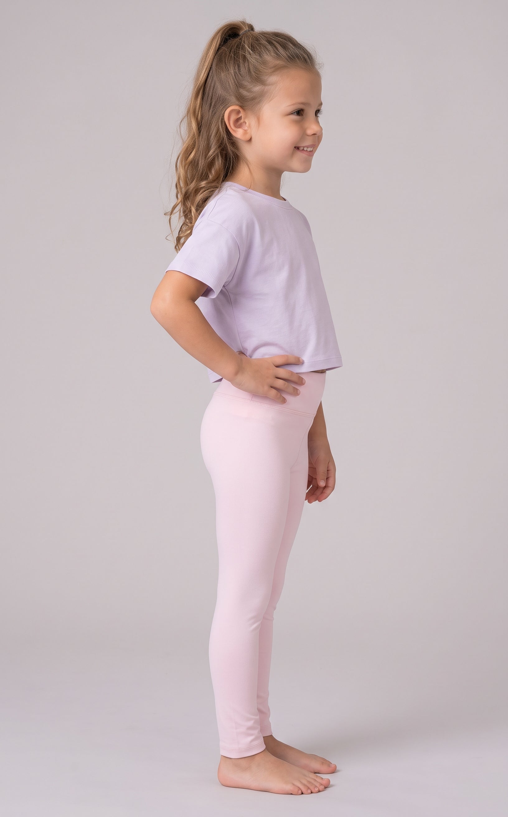Little girl modeling full-length pale pink leggings with a matching loose T-shirt, shown in side profile.