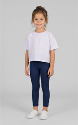 Toddler girl wearing solid light purple short-sleeve t-shirt with navy blue fitted leggings and white sneakers on gray.