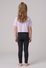 A girl models full-length black leggings with a lavender short-sleeve top, shown from behind.