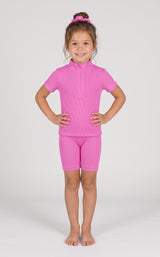 Toddler wearing a bright pink ribbed short-sleeve top and matching fitted shorts, hands on hips.