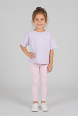Toddler wearing pale pink leggings with a loose lavender T-shirt and white sneakers.