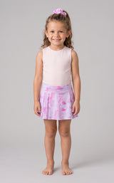 Little girl wearing a sleeveless white tank top with a fuchsia pink tie-dye pleated skort and matching scrunchie in her.