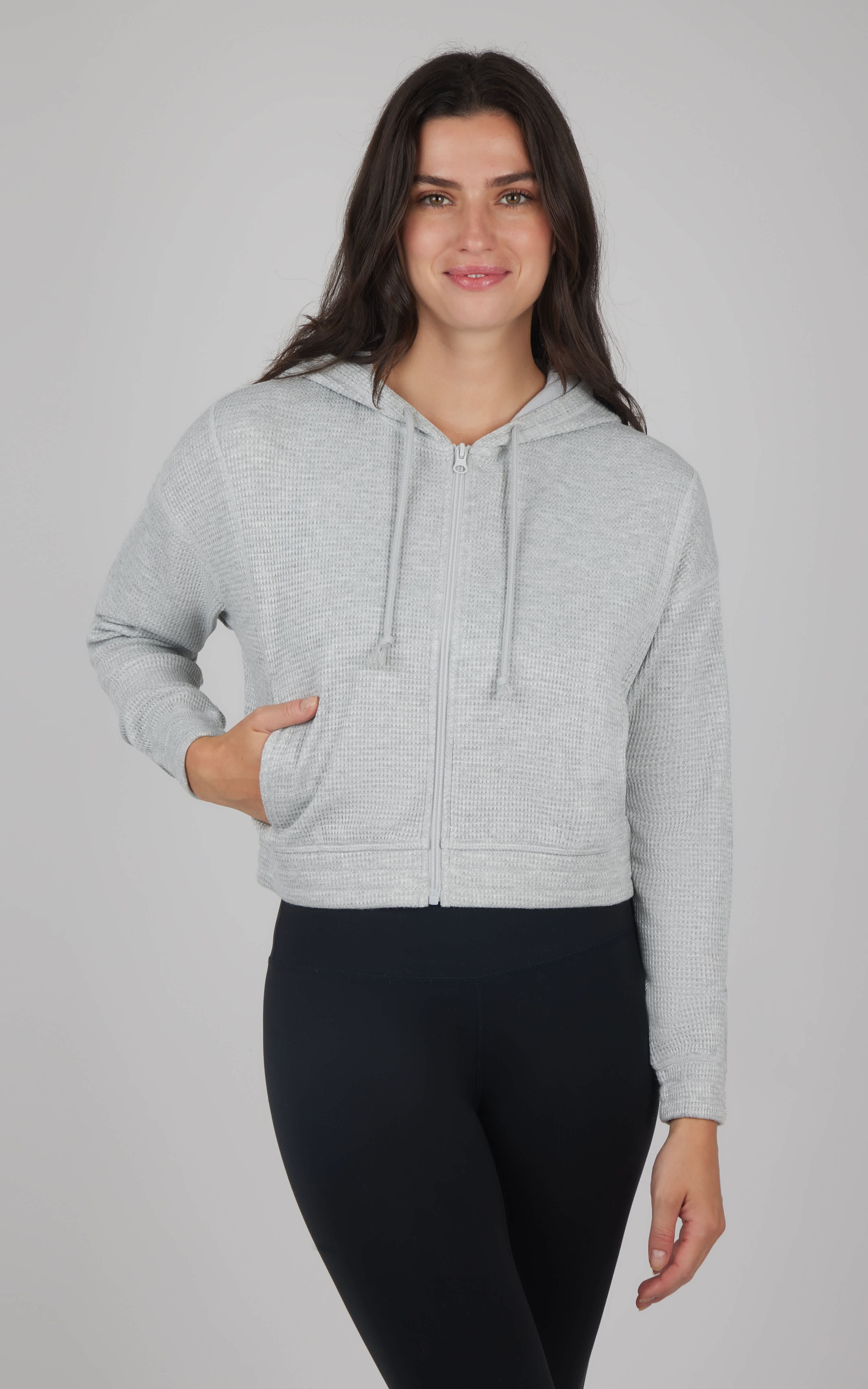 Heather grey cropped hoodie jacket with kangaroo pocket and drawstring hood worn with black leggings.