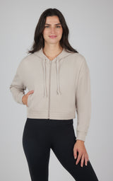 Woman wearing a beige hooded jacket with a full-length zipper, drawstrings, and front pockets over black leggings.