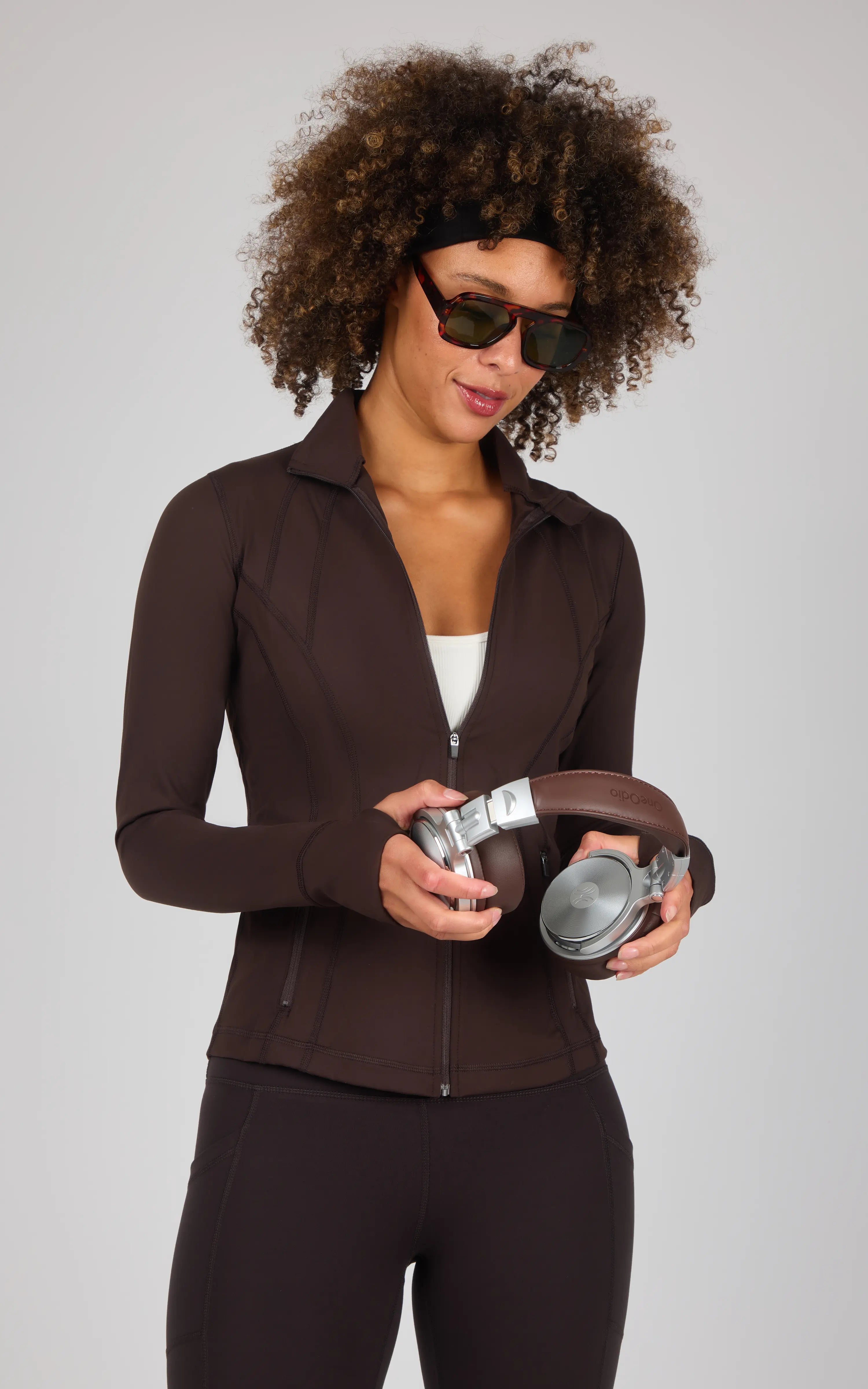Dark brown full-zip runner jacket with high collar and fitted silhouette worn with matching leggings.