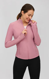 Woman wearing a fitted pink ribbed full-zip jacket with a mock neck, long sleeves, and thumbholes.