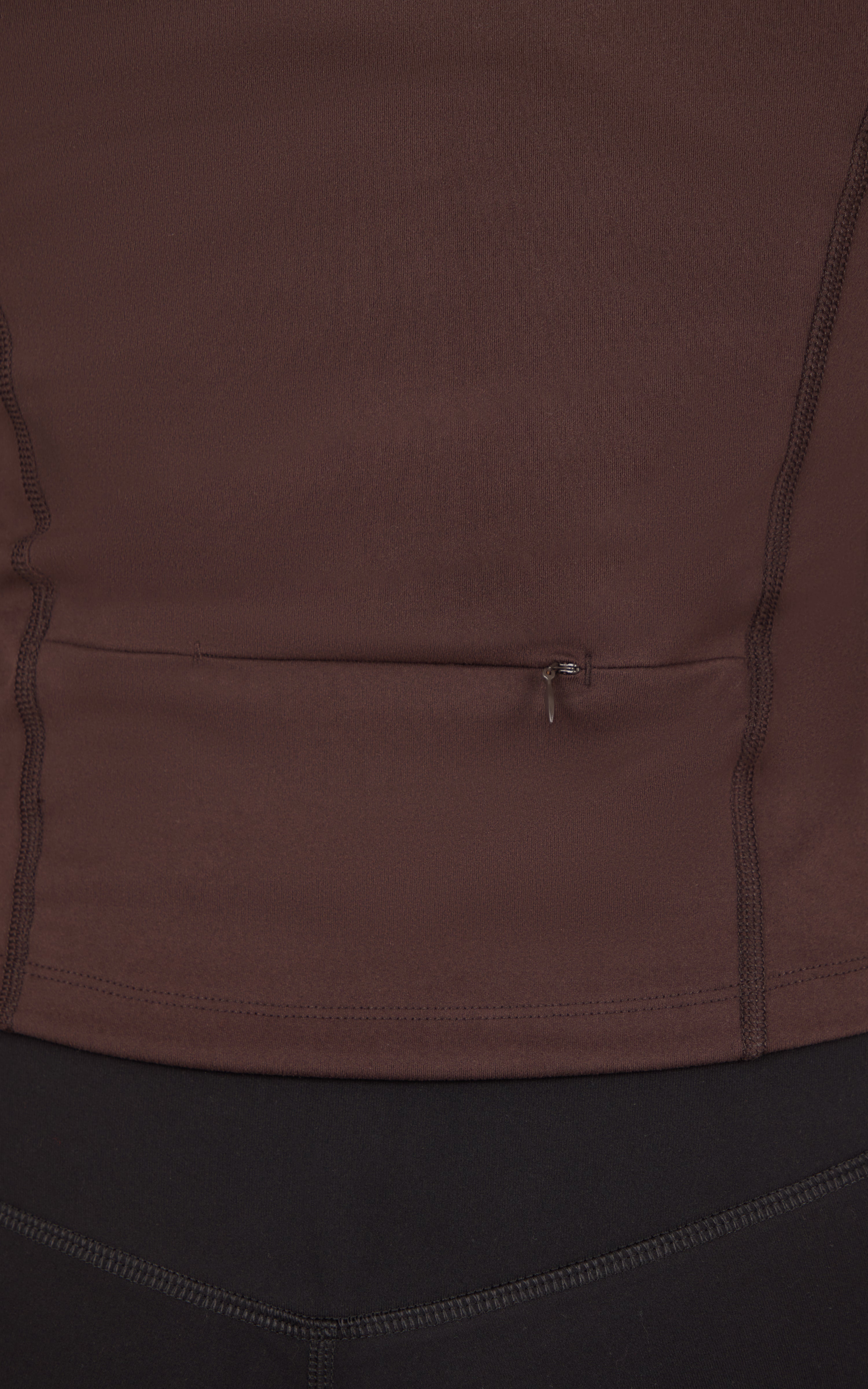 Close-up of a dark brown jacket with a horizontal zippered chest pocket and curved seam detailing.