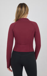 Back view of a burgundy long-sleeve raglan jacket with a raised collar and fitted waist, paired with black pants.
