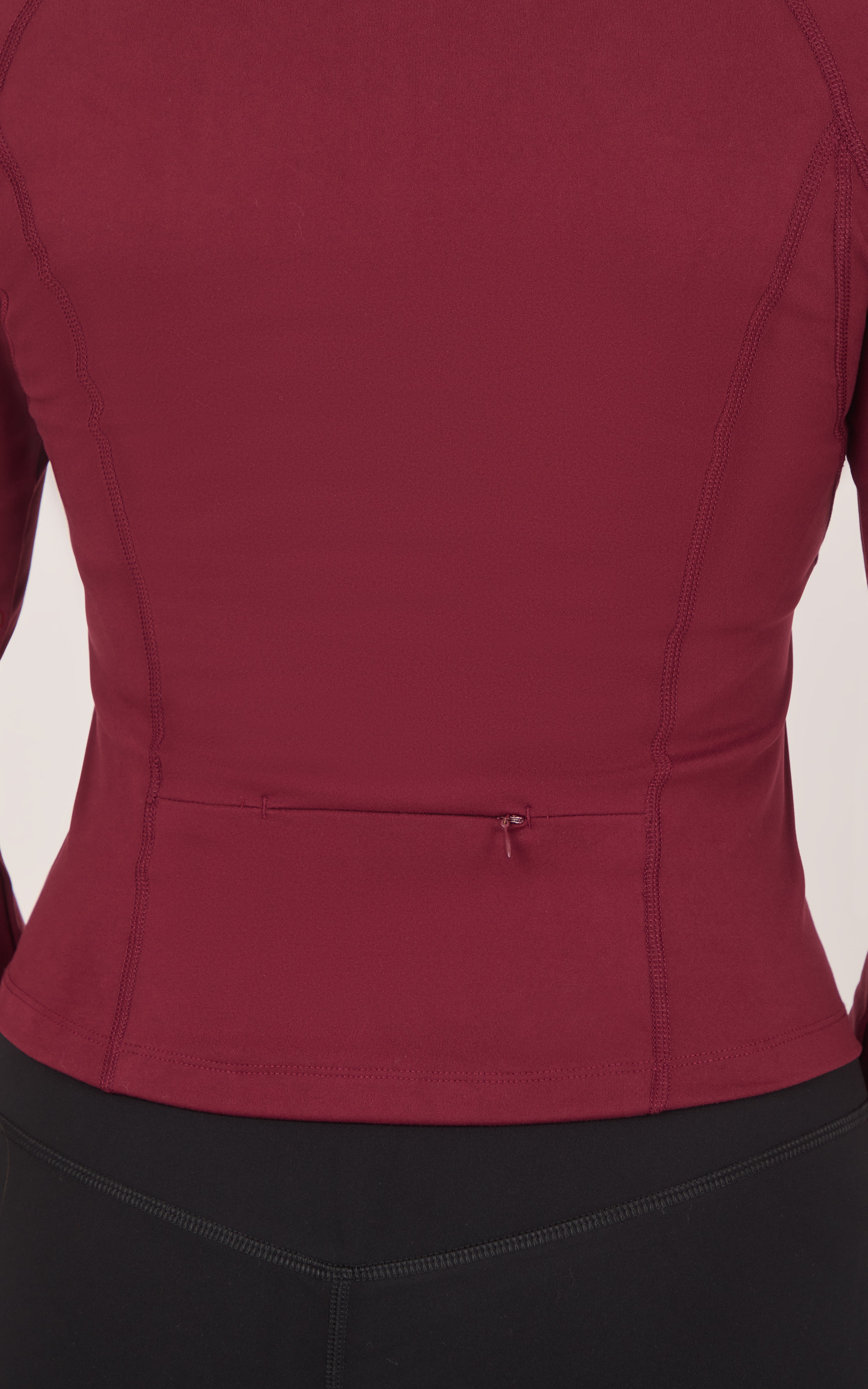 Burgundy raglan jacket with a fitted waist seam and small center-back fastening, shown above black bottoms.