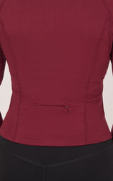 Burgundy raglan jacket with a fitted waist seam and small center-back fastening, shown above black bottoms.