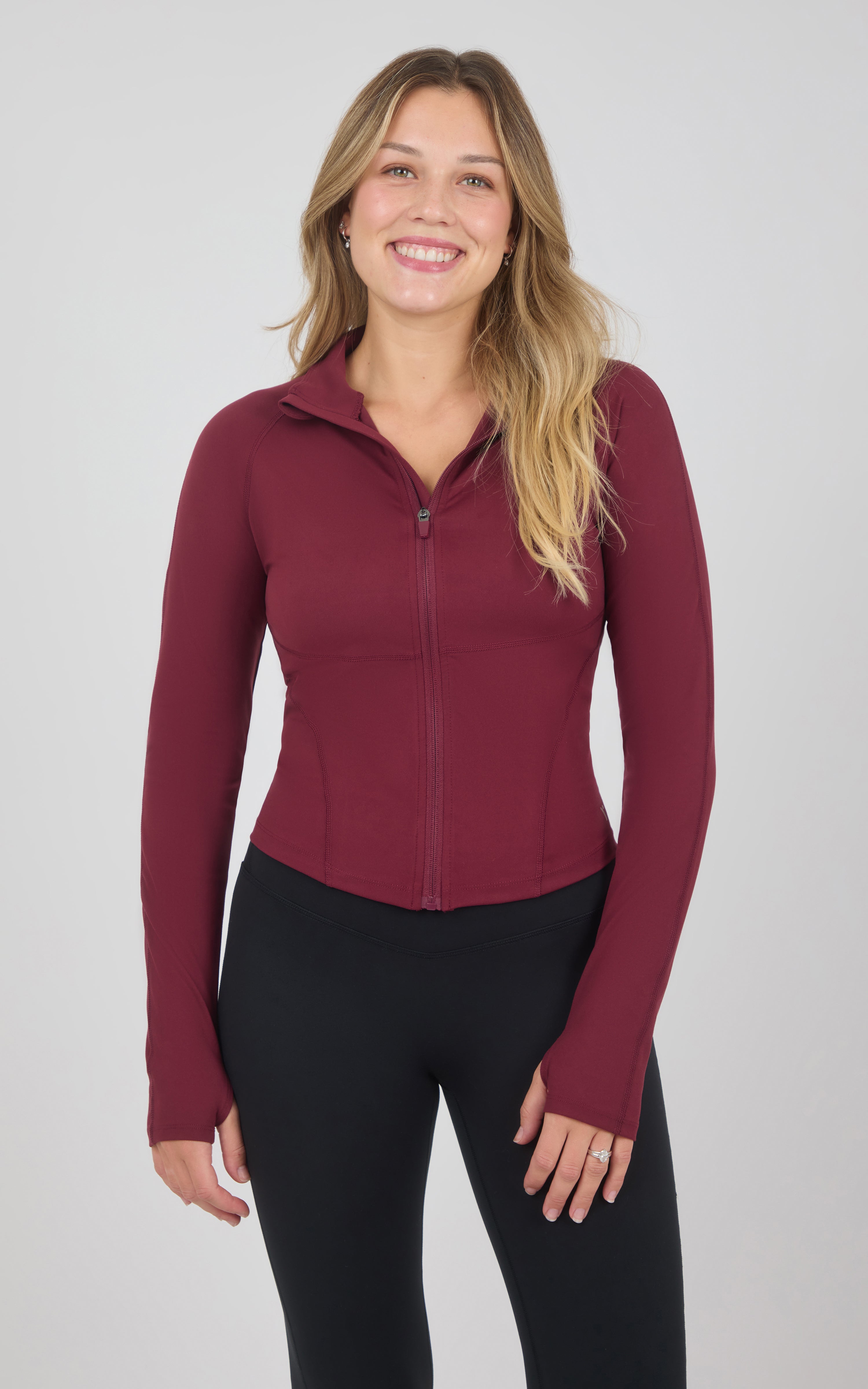 Burgundy full-zip raglan jacket with a fitted silhouette, stand collar, and long sleeves, paired with black pants.