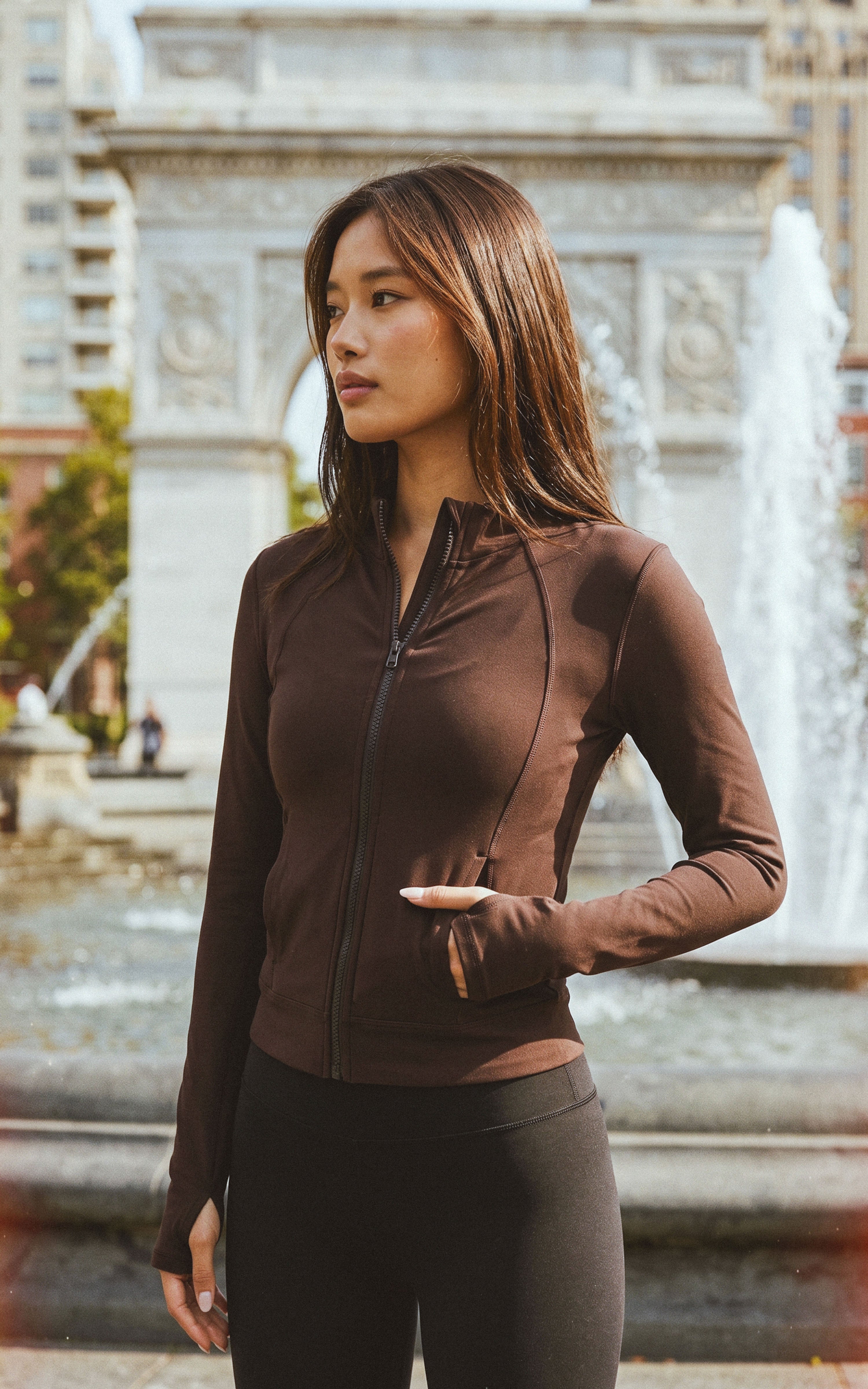 Women's full zip athletic jacket in deep brown with thumbholes and fitted silhouette.