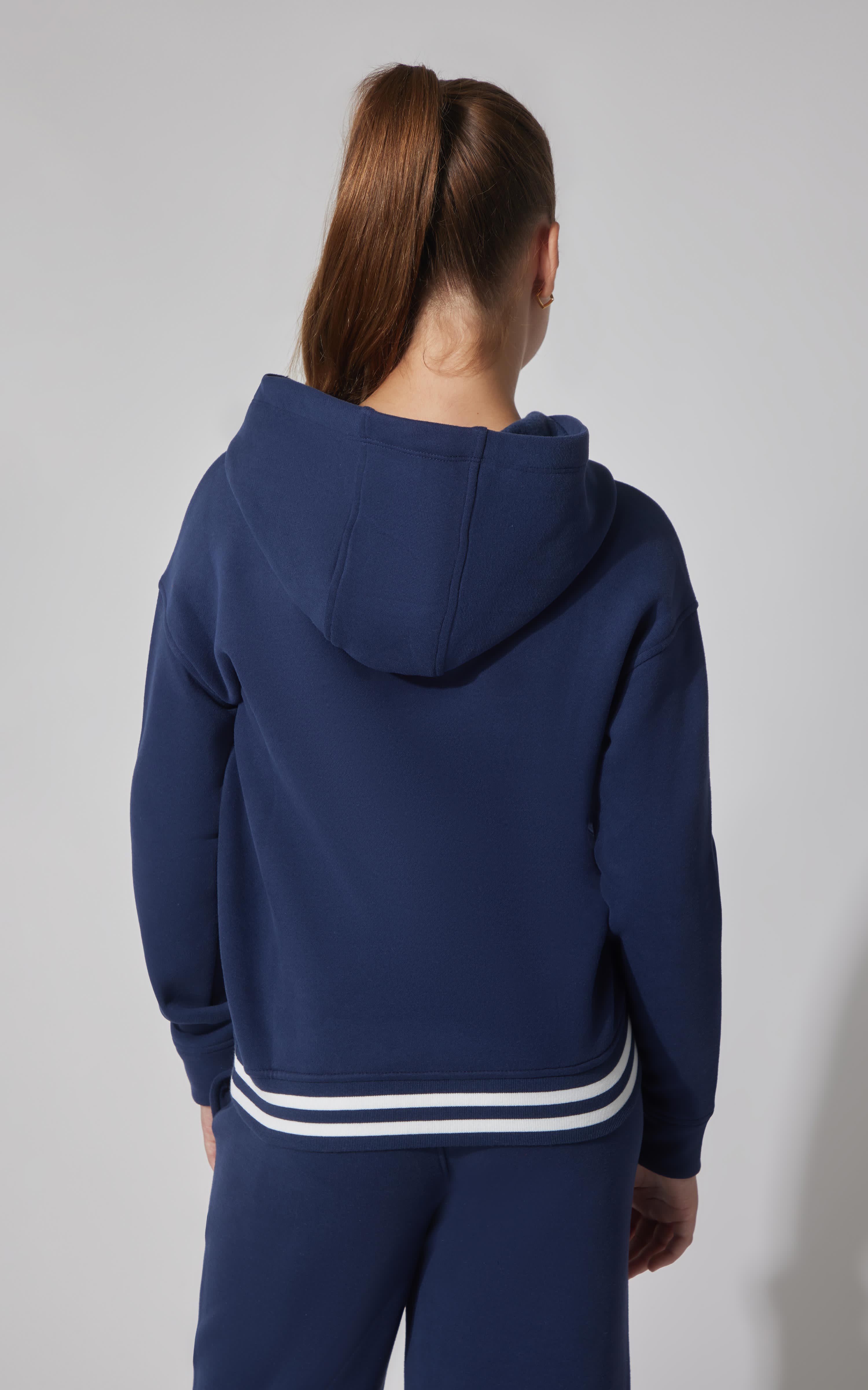 Navy blue fleece pullover hoodie with attached hood and white striped hem on girl model back view.