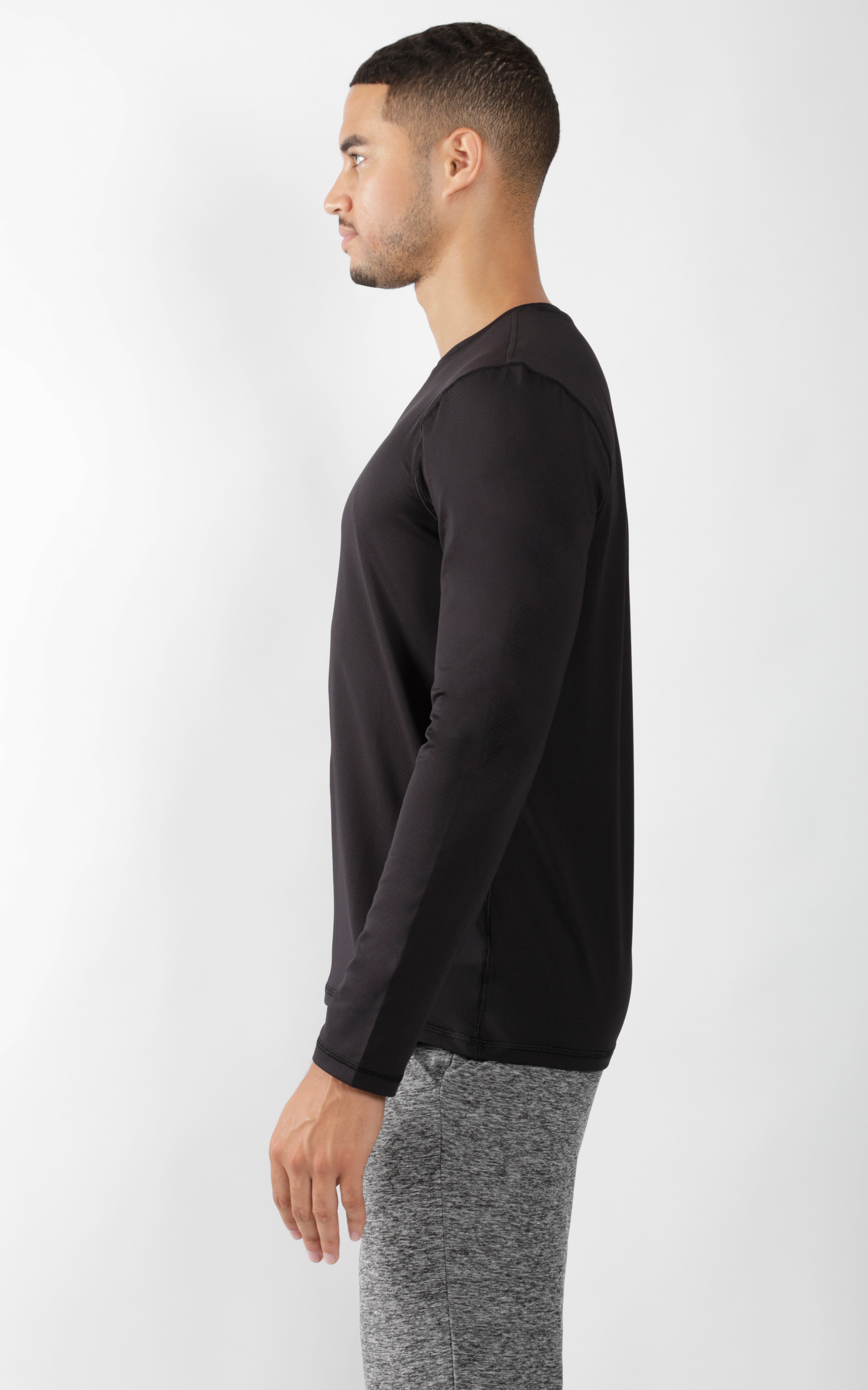 Men's black crew neck long sleeve shirt paired with grey knit pants, side view.