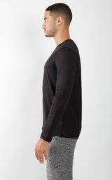 Men's black crew neck long sleeve shirt paired with grey knit pants, side view.