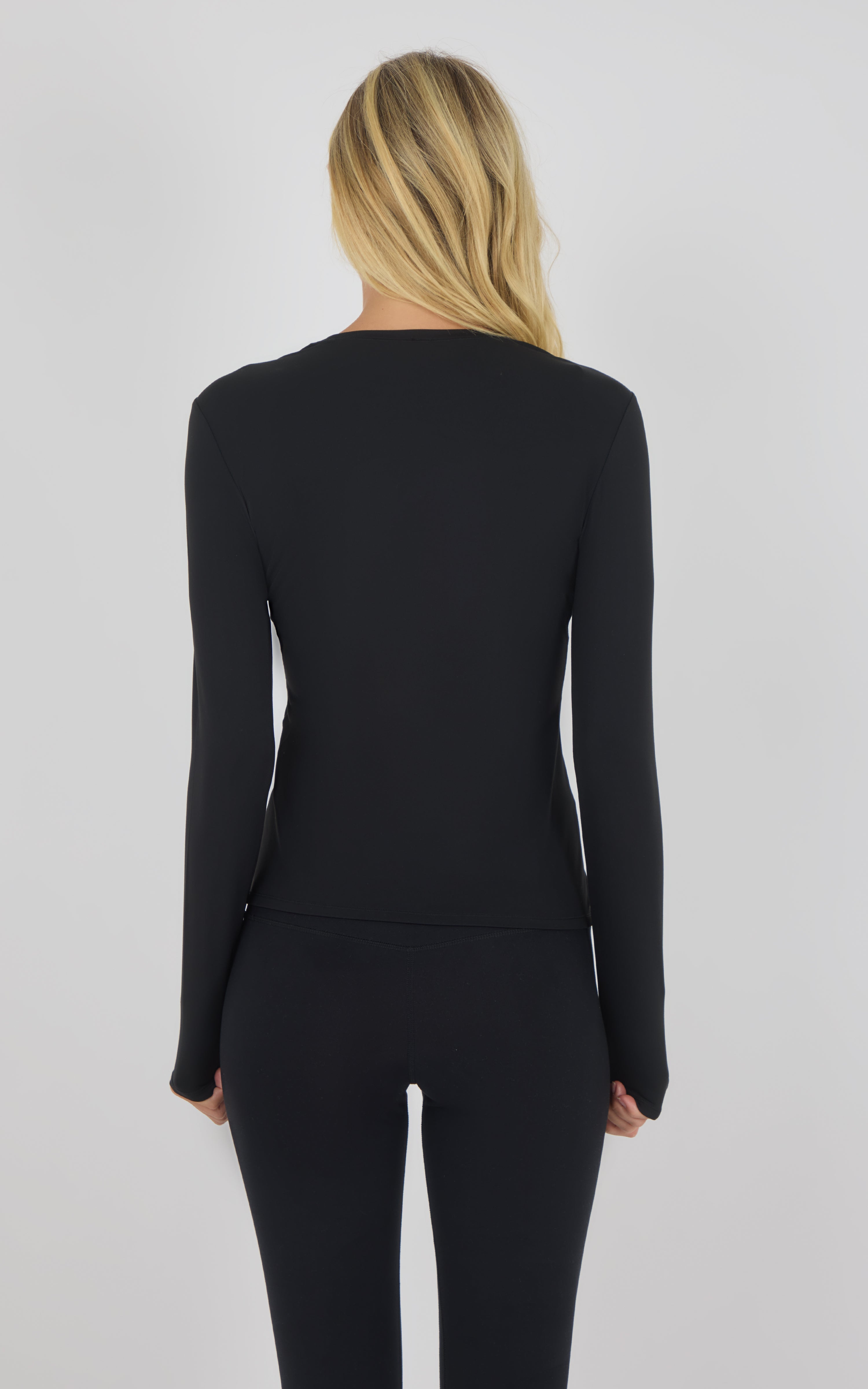 Black long sleeve fitted top with crew neck, smooth fabric, and thumbholes at cuffs.