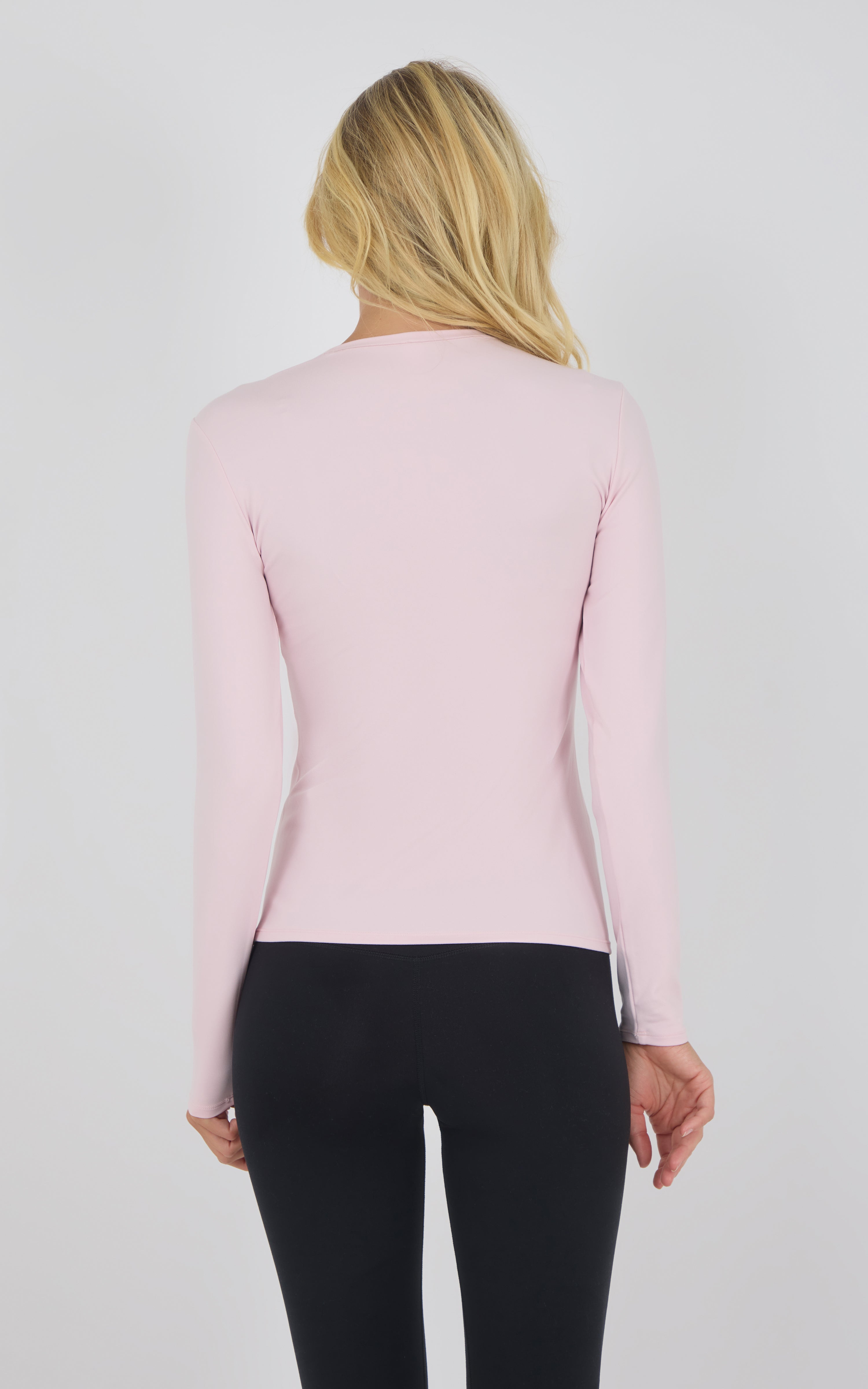 Chalk pink long sleeve fitted top with crew neck on woman facing away.
