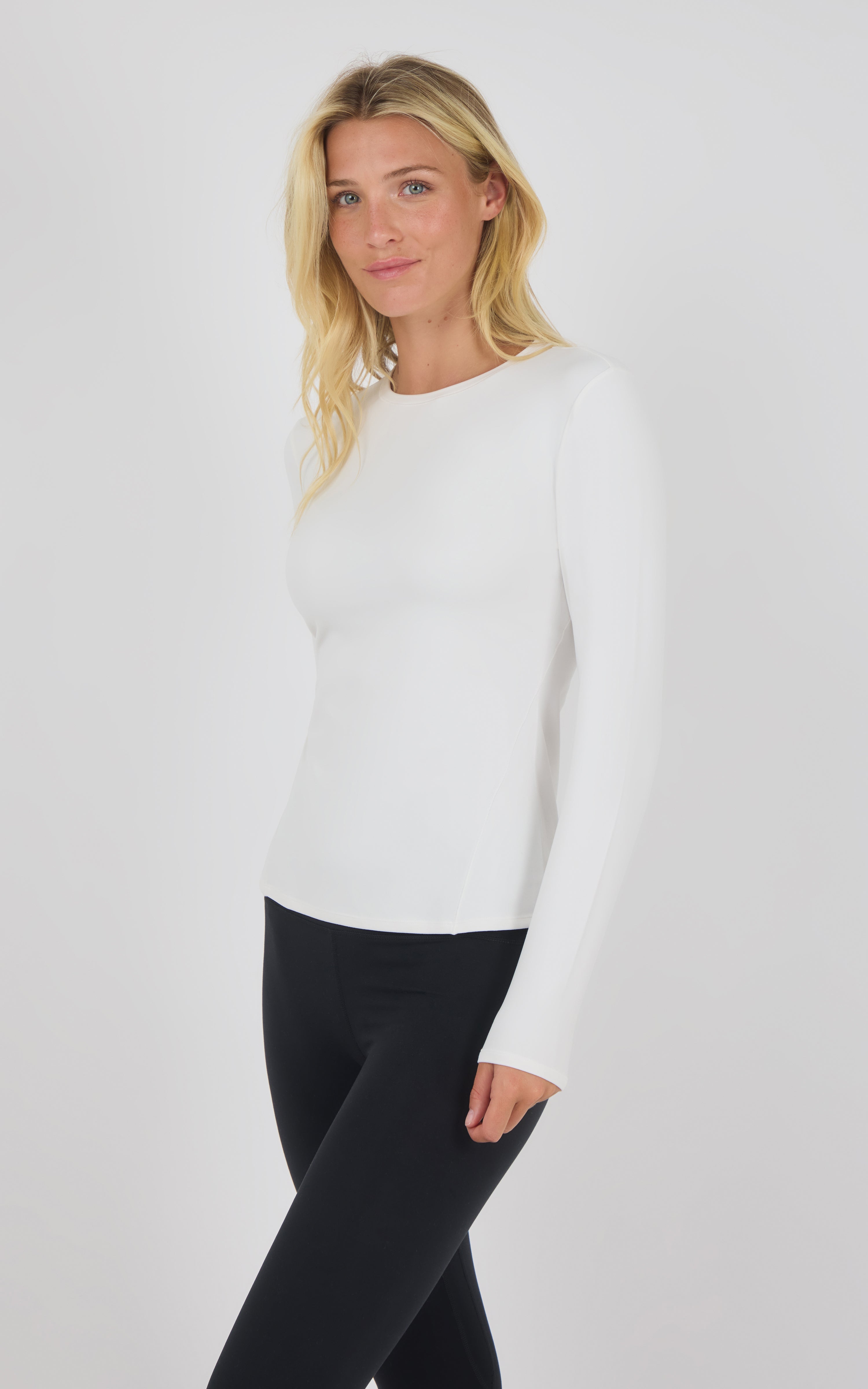 White fitted long sleeve top with crew neck on a model wearing black pants.