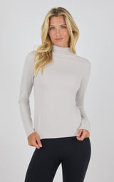 Light taupe mock neck long sleeve top with fitted silhouette on woman.