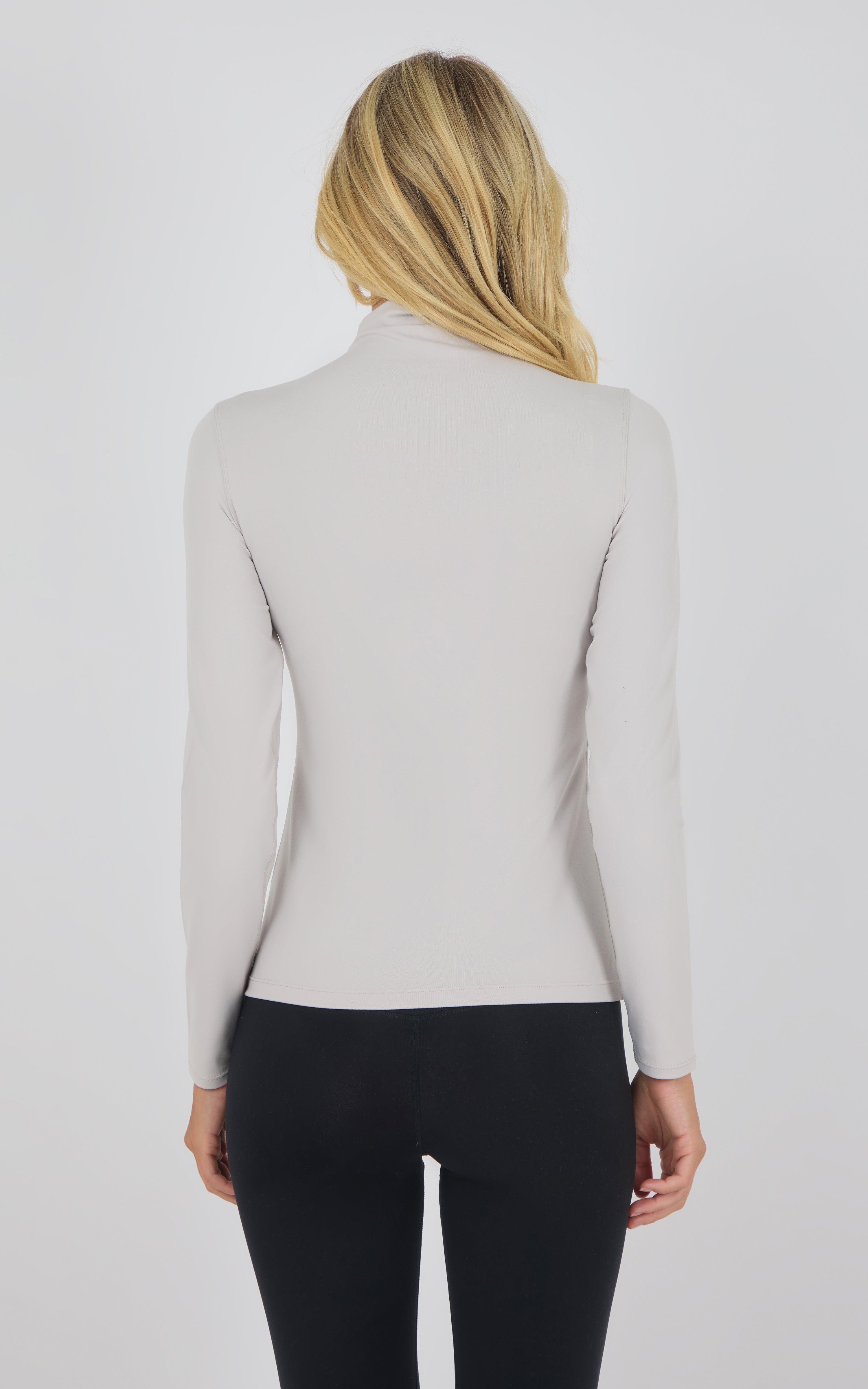 Light beige mock neck long sleeve top with slim fit, worn with black pants, back view.