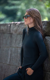 Black mock neck long sleeve top styled with sunglasses against a stone wall background.