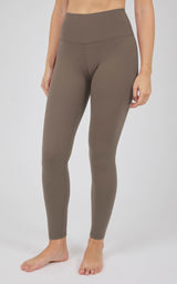Woman wearing full-length, high-rise taupe leggings with a smooth, close-fitting silhouette and tapered ankles.