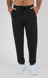 Black men’s jogger pants with a drawstring waist, tapered cuffs, and a soft, smooth finish, styled with white sneakers.