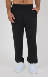 Black soft fabric joggers with elastic waistband and tapered legs, worn with white sneakers.