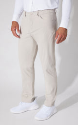 A person wearing light beige chinos or casual trousers with a white long-sleeve shirt and white sneakers, shown from the waist down against a light gray studio background.