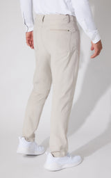 A person shown from the back wearing light beige trousers, a white long-sleeve shirt, and white sneakers against a plain light gray studio background.