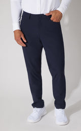 A man wearing navy blue dress pants, a white long-sleeve shirt, and white sneakers, shown from the waist down against a light gray studio background.
