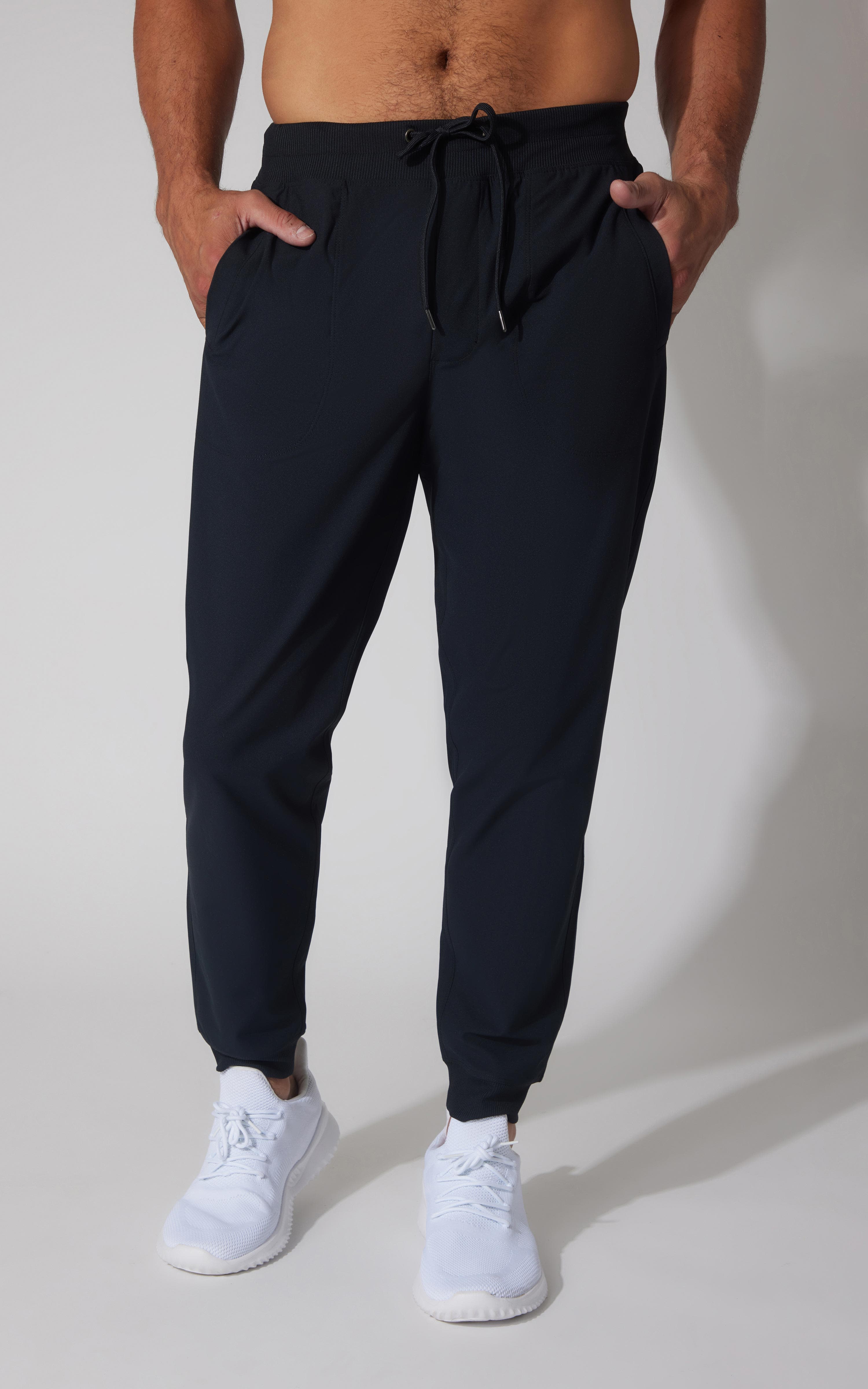 Men's true navy tricot joggers with elastic cuffs and drawstring waist, styled with white sneakers.