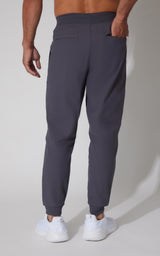 Men's dark gray tricot joggers with elastic cuffs and back pocket, paired with white sneakers.