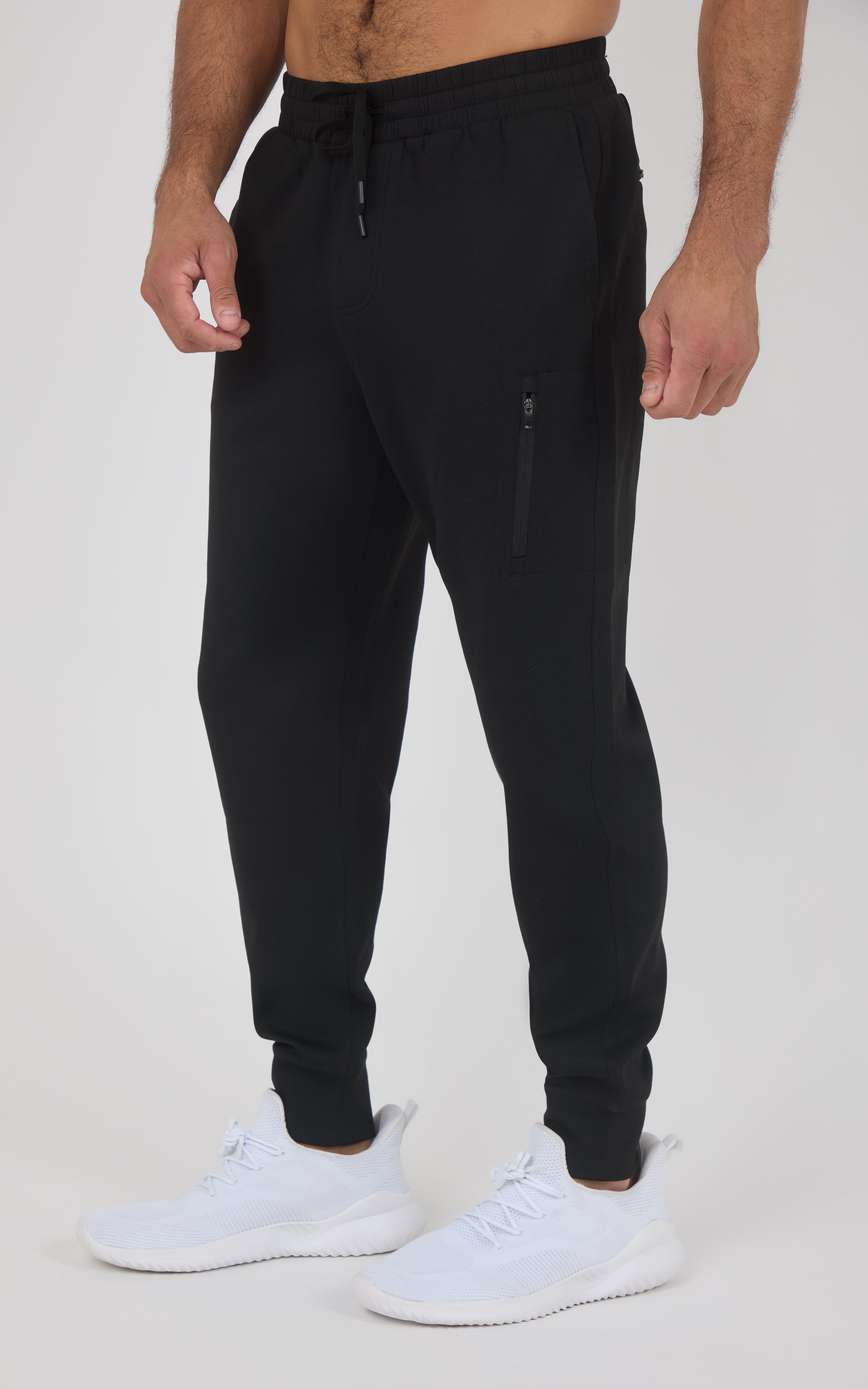 Black slim-fit joggers with elastic waistband and ankle cuffs, zippered side pocket, worn with white sneakers.