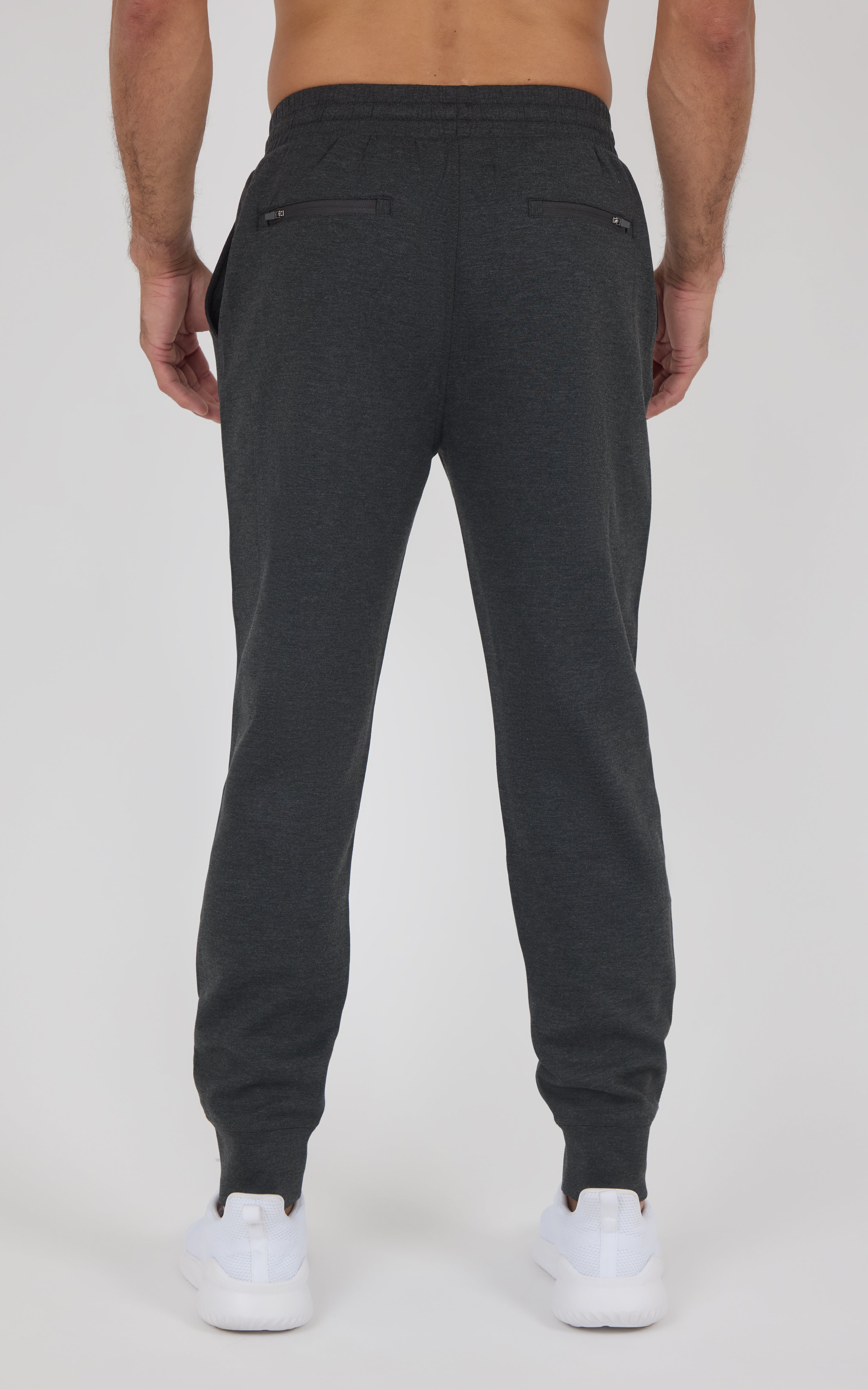 Dark gray slim-fit joggers with elastic cuffs and back zip pocket, worn with white sneakers.