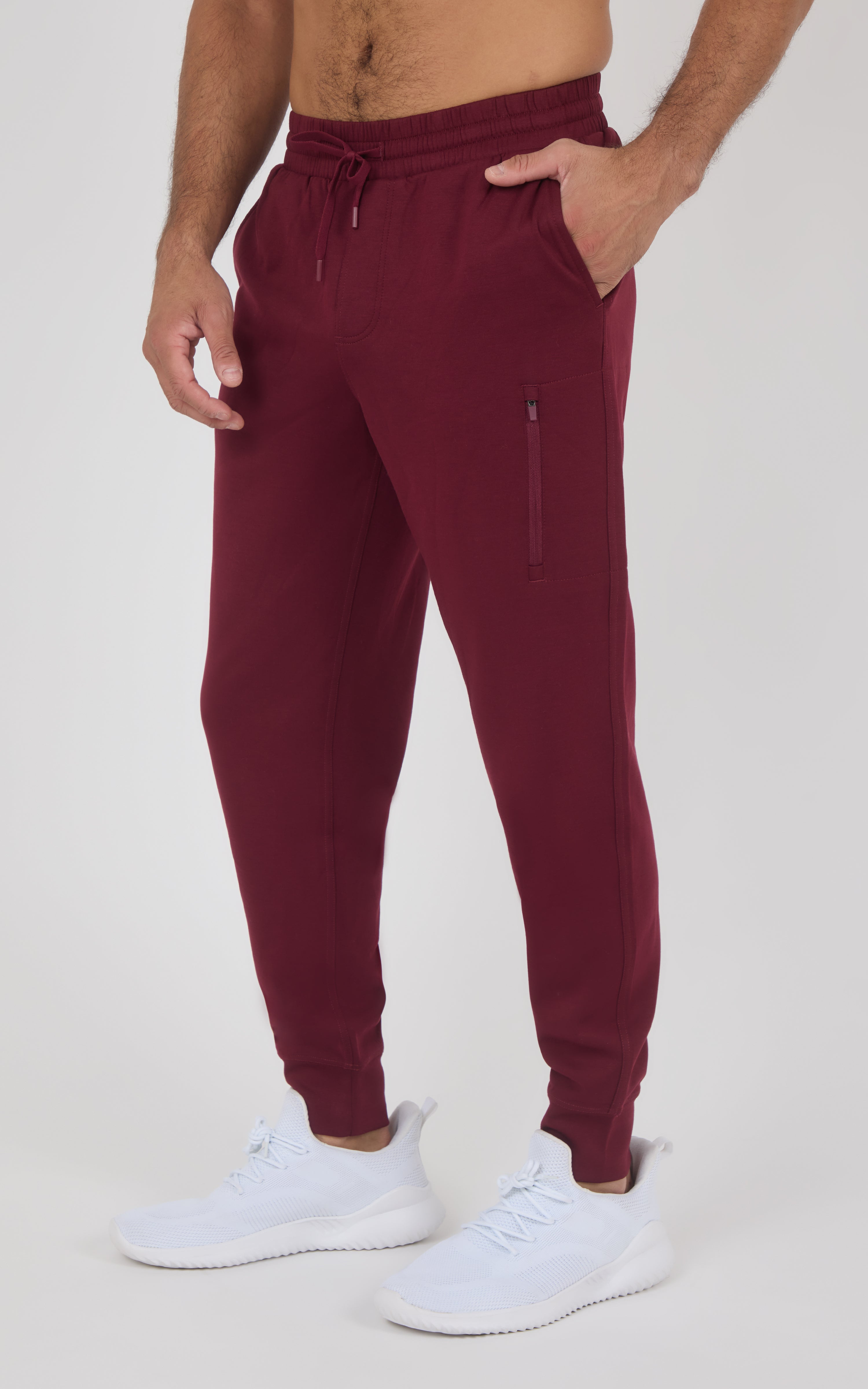 Burgundy slim-fit joggers with elastic waistband, side zipper pocket, tapered legs, and cuffed ankles, worn with white.