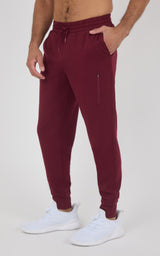 Burgundy slim-fit joggers with elastic waistband, side zipper pocket, tapered legs, and cuffed ankles, worn with white.