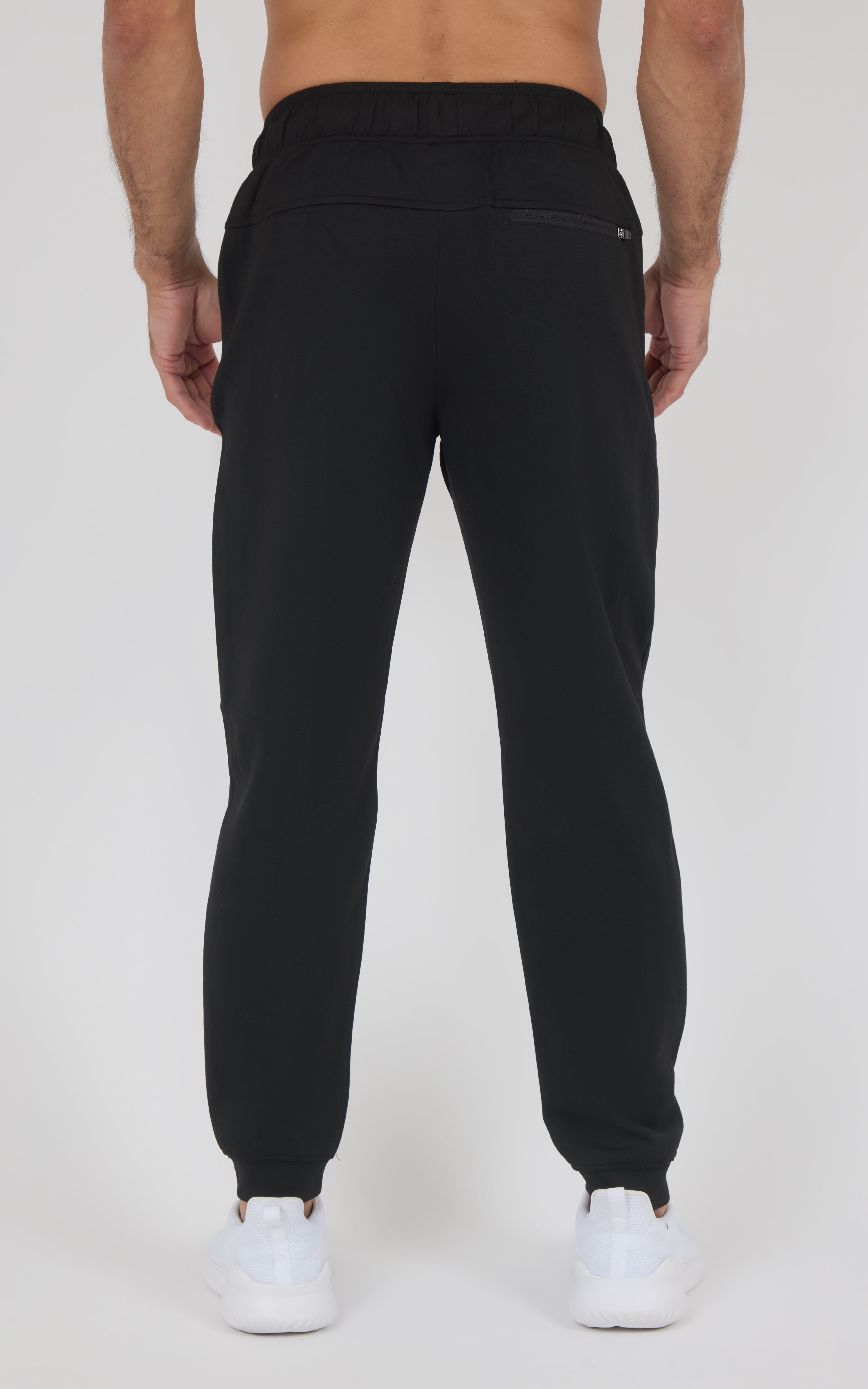 Back view of black jogger pants with a smooth, tapered fit, elastic cuffs, and a rear pocket, paired with white sneakers.