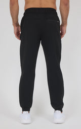 Back view of black jogger pants with a smooth, tapered fit, elastic cuffs, and a rear pocket, paired with white sneakers.