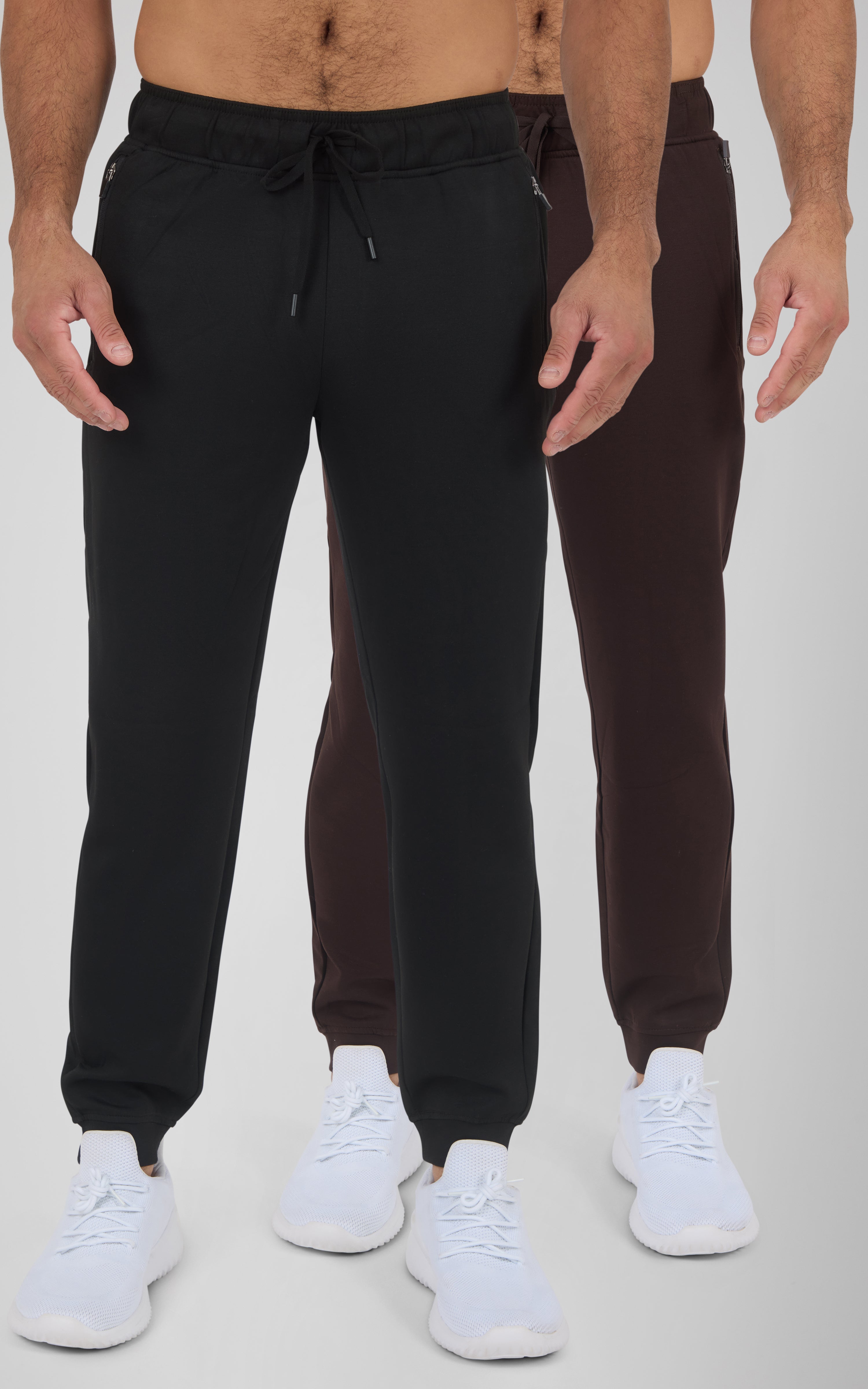 Black and dark brown men's joggers with elastic waistbands, tapered legs, and white sneakers.