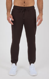 Dark brown men’s jogger pants with a drawstring waist, tapered legs, and elastic cuffs, styled with white sneakers.